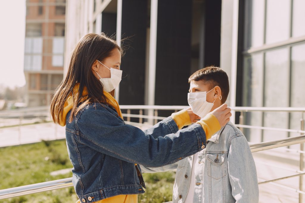 Girl in medical mask fixing boy's medical face mask